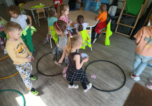 Dzieci wykonują zadanie edukacyjne z wykorzystaniem obrazków i kół hula-hop.