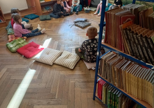 Dzieci siedzą w bibliotece na poduchach.