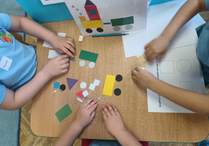 Troje dzieci przy stoliku układa obrazek z figur geometrycznych według wzoru.