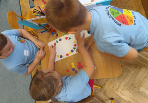 Dzieci układają rytm z figur geometrycznych na kartce papieru.