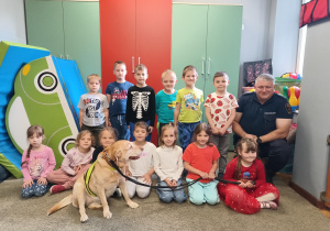 Zdjęcie grupowe dzieci z grupy IV wraz z funkcjonariuszem Straży Miejskiej i psem.