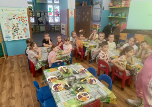Przedszkolaki siedzą przy stolikach i słuchają ciekawostek na temat herbat z całego świata.