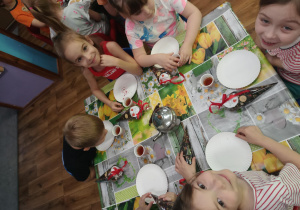 Dzieci siedzą przy stoliku i jedzą ciasteczka popijając herbatę.