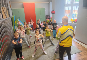 Dzieci stoją na dywanie i uczestniczą w zajęciach karate.