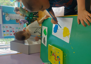 Dwóch chłopców rozdmuchuje farbę na kartce papieru.