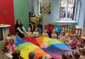 Dzieci w kręgu trzymają chustę animacyjną, na której podrzucają różowego balona.