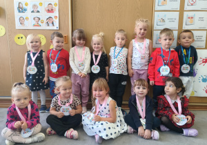 Uśmiechnięte dzieci pozują do zdjęcia. Każde dziecko ma na szyi medal, który otrzymało z okazji Dnia Kropki.