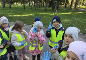 Dzieci stoją w parku ubrane w odblaskowe kamizelki i szykują się do sprzątania parku.