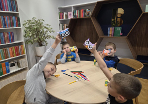 Czterech chłopców siedzi przy okrągłym stoliku i pokazują papierowe sowy, które sami zrobili.