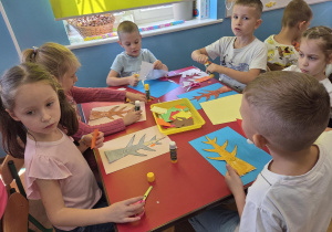 Dzieci siedzą przy stoliku i wykonują pracę plastyczną "Jesienne drzewo".