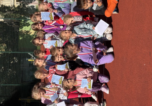 Grupa dzieci na boisku szkolnym. Każde z dzieci trzyma dyplom, a na szyi ma medal.