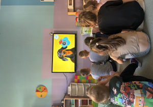 Dzieci siedząc na dywanie oglądają film edukacyjny "Mój przyjaciel pies".