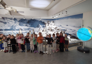 Dzieci pozują do zdjęcia. Z tyłu widać ekspozycję muzealną z pingwinami.