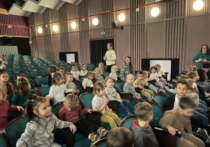 Dzieci w sali teatralnej czekają na rozpoczęcie przedstawienia.