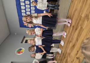 Cztery dziewczynki stoją na środku sali. Jedna dziewczynka mówi wiersz do mikrofonu.