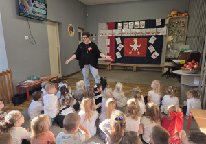 Dzieci siedzą na dywanie i słuchają nauczycielki, która opowiada im o Dniu Niepodległości.