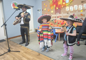 Mariachi gra na meksykańskiej gitarze vihuela, a dwoje dzieci w meksykańskich sombrero gra na marakasach.
