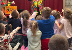 Dzieci siedząc na dywanie czarują za pomocą rączek.