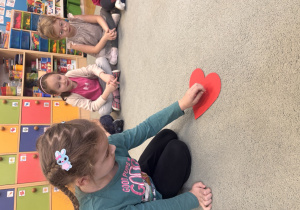 Dziewczynka przekłuwa pinezką papierowe serce, na którym napisane są imiona chłopców.