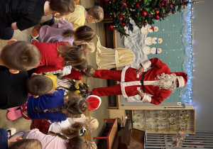 Święty Mikołaj opowiada dzieciom o tym jak przyjechał do przedszkola. Dzieci siedzą na dywanie i słuchają.