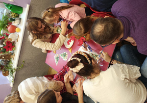 Rodzice z dziećmi wykonują przy stolikach lampiony ze słoików.