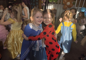 Dziewczynki przebrane za Kopciuszka i Biedronkę przytulają się pozując do zdjęcia.