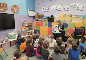 Dzieci siedzą na dywanie i słuchają prelekcji funkcjonariuszki Straży Miejskiej.