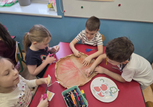 Dwóch chłopców koloruje szablon pizzy, dwie dziewczynki wycinają składniki z papieru.