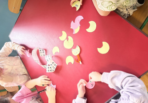 Dzieci siedzą przy czerwonym stoliku i tworzą kotki.