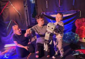 Chłopiec z aktorami stoi na scenie, w ręku trzyma robota.