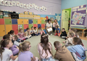 Dzieci siedzą w kręgu na dywanie. Wśród nich siedzą Panie psycholog i logopeda.