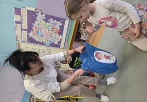 Pani logopeda podaje dziewczynce niebieski worek złości, w który dziewczynka wrzuca zgnieciony papier.