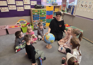 Dzieci z nauczycielką siedzą na dywanie wokół globusa.