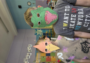 Dziewczynka i chłopiec w maskach dinozaurów.