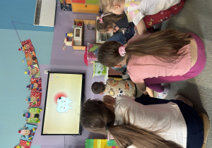 Dzieci siedząc na dywanie oglądają prezentację dotyczącą higieny jamy ustnej.