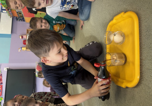 Chłopiec nalewa coli do szklanki, w której znajduje się jajko.