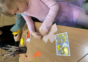 Dziewczynka siedzi przy stoliku i składa papierowe pudełko.