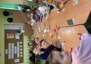 Grupa dzieci siedzi przy stolikach i wykonują wiosenne kartki.