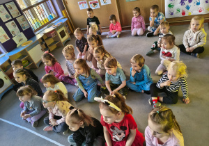 Dzieci siedzą na dywanie i oglądają prezentację.