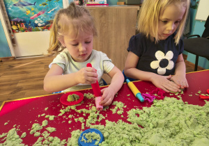 Dwie dziewczynki bawią się piaskiem kinetycznym.