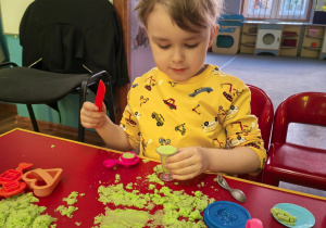 Chłopiec bawi się zielonym piaskiem kinetycznym.