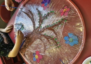 Dzieci malują farbą na folii rozciągniętej na hula-hop.