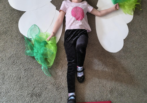 Dziewczynka tworzy "żywy obraz" na kształt kwiatka w doniczce.