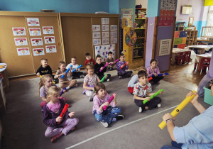 Dzieci siedzą na dywanie, w rękach trzymają kolorowe rurki.