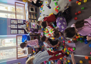 Dzieci za pomocą szufelek, sprzątają z dywanu kolorowe piłki.