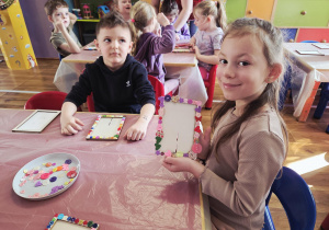 Dziewczynka przy stoliku prezentuje własnoręcznie ozdobioną ramkę na zdjęcia.