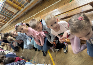 Przedszkolaki siedzą na ławce i czekają na rozpoczęcie przedstawienia.