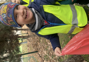 Chłopiec w kamizelce odblaskowej trzyma worek ze śmieciami.