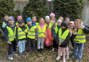 Grupa dzieci w kamizelkach odblaskowych pozuje do zdjęcia.