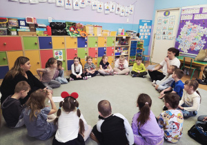 Dzieci siedzą w kręgu na dywanie.